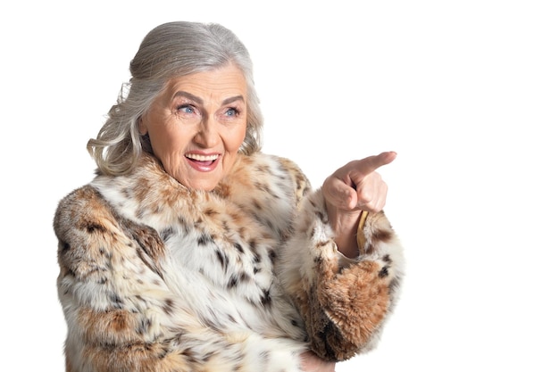 Starsza kobieta w futrze wskazuje palcem na coś za ramą na białym tle