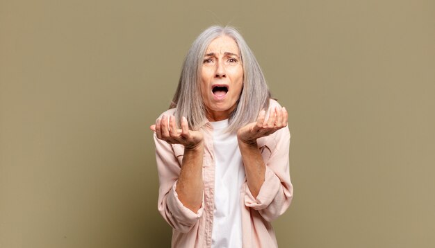 Starsza kobieta wyglądająca na zdesperowaną i sfrustrowaną, zestresowaną, nieszczęśliwą i zirytowaną, krzyczy i krzyczy