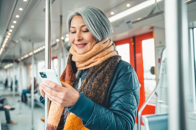 Starsza kobieta wysyła wiadomość za pomocą telefonu komórkowego w pociągu