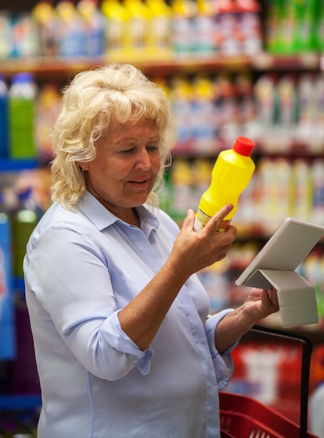 Zdjęcie starsza kobieta z padem czyta detergentową etykietkę