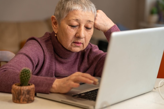 starsza kobieta z siwymi włosami siedzi przy laptopie robi zakupy online lub pracuje