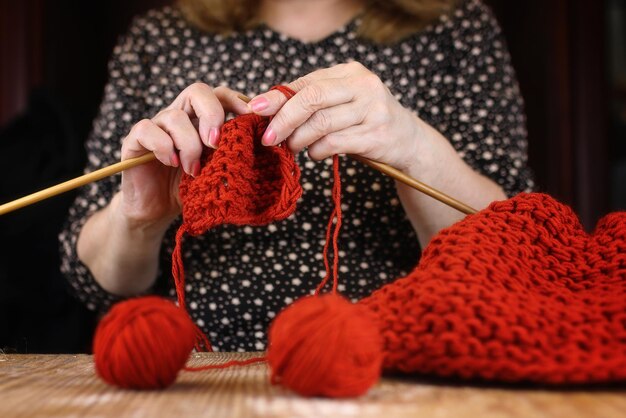 Starsza kobieta zajmuje się robieniem na drutach ciepłych swetrów dla wnuków