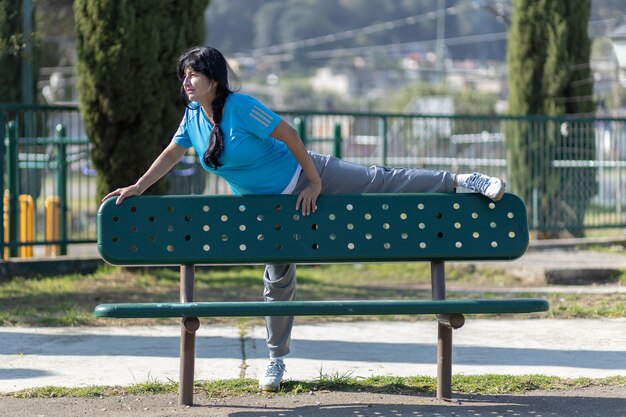 Starsza meksykańska kobieta rozciągająca się na ławce w parku, trening miejski
