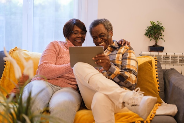 Starsza para razem na kanapie za pomocą tabletu i komunikująca się z rodziną online