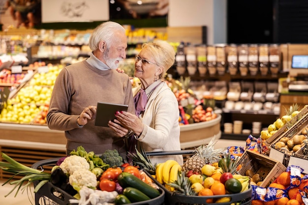 Starsza para śledzi listę na tablecie i kupuje artykuły spożywcze w supermarkecie