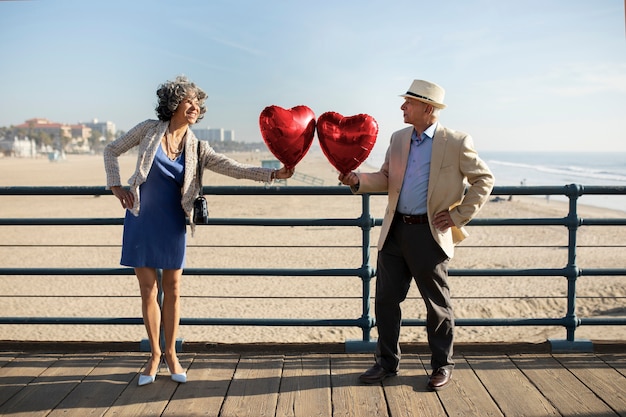 Zdjęcie starsza para trzymająca balony w kształcie serca podczas randki na plaży