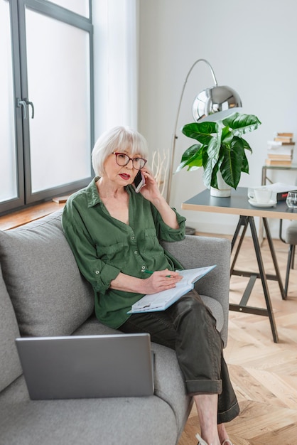starsza przyjazna kobieta przedsiębiorca pracuje w domu rozmawia przez telefon pracuje z laptopem