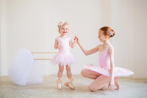 Starsza siostra, baletnica w różowej tutu i butach pointe, pokazuje dziecku, jak ćwiczyć przy drążku