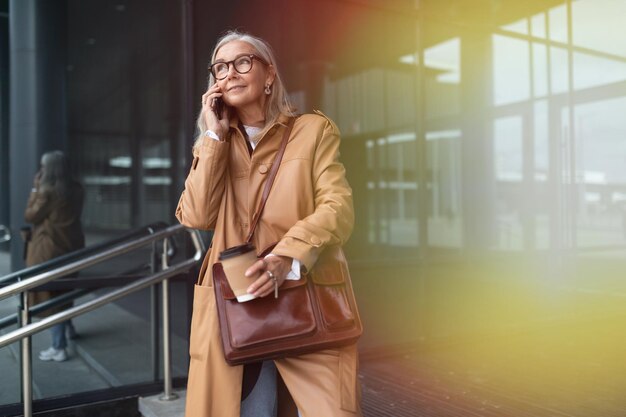Starsza stylowa kobieta rozmawia przez telefon komórkowy obok centrum handlowego