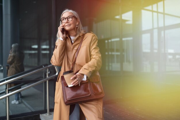 Starsza stylowa kobieta rozmawia przez telefon komórkowy obok centrum handlowego