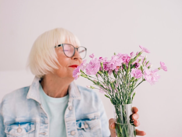 Starsza Stylowa Kobieta W Okularach I Dżinsowej Kurtce Pachnie Kwiatami Goździka W Wazonie