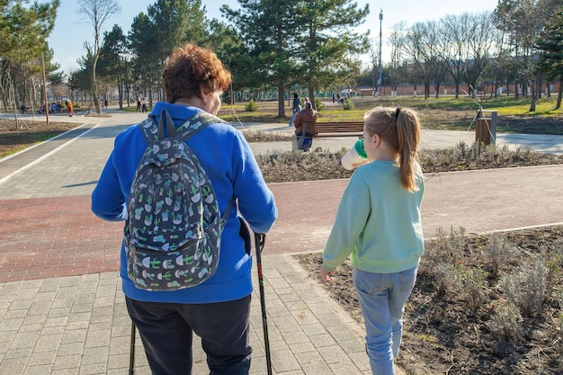 Starsza wysportowana kobieta spaceruje po parku w słoneczny dzień ze swoją wnuczką