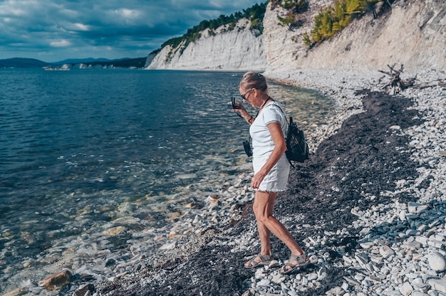 Starsze osoby starsze, podróżujące z plecakiem, starsza kobieta, turysta, pieszy, robić zdjęcia na wybrzeżu