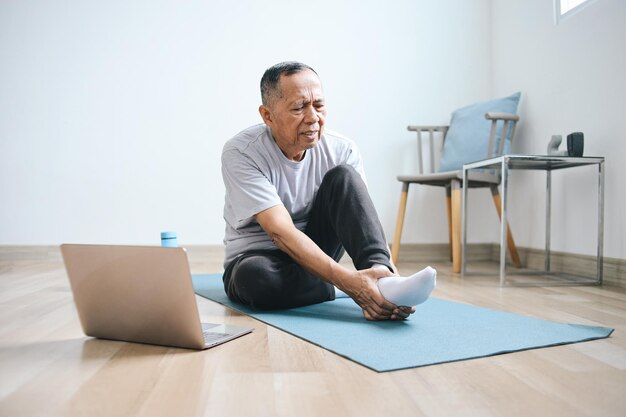 Starszy azjatycki mężczyzna dotykający stóp cierpiący z powodu bólu podczas ćwiczeń w domu Koncepcja podiatryczna