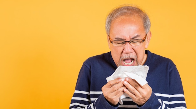 Starszy azjatycki mężczyzna przeziębiony z grypą i kichający z powodu problemu z wirusem choroby używa tkanki