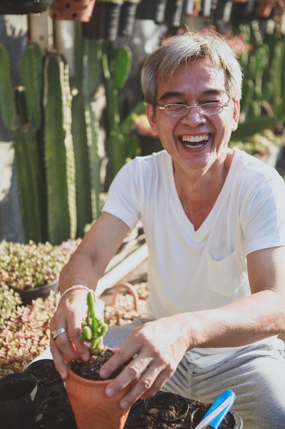 Zdjęcie starszy azjatycki mężczyzna śmiejący się ze szczęścia podczas sadzenia soczystej rośliny