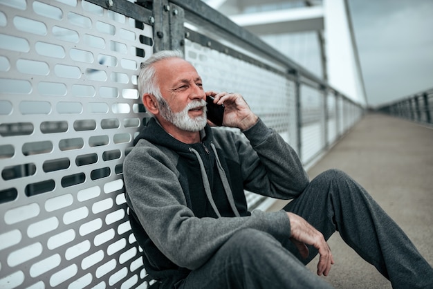 Starszy biegacz odpoczywa i rozmawia przez telefon komórkowy w mieście.