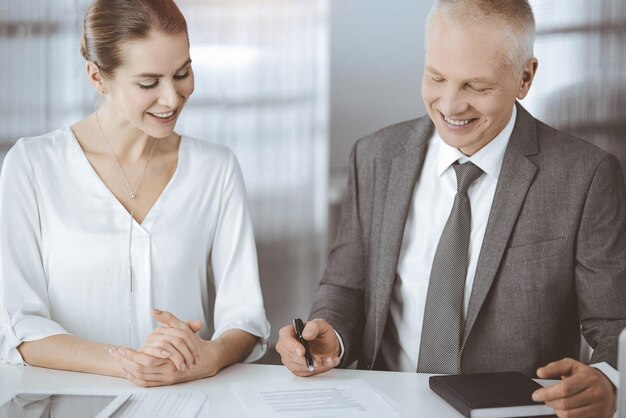 Starszy biznesmen i kobieta siedzi i komunikacji w słonecznym biurze. Dorośli ludzie biznesu lub prawnicy pracujący razem jako partnerzy i koledzy na spotkaniu.