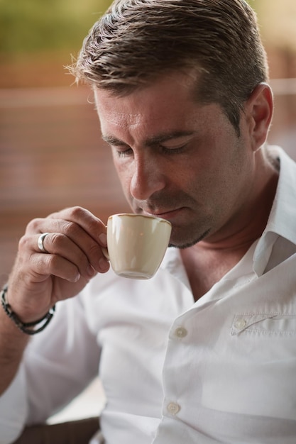 Starszy biznesmen w codziennych ubraniach siedzi na tarasie luksusowego domu i pije poranną kawę