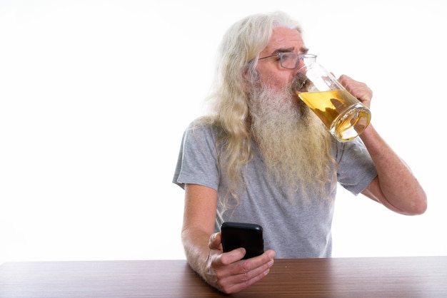 starszy brodaty mężczyzna trzyma telefon komórkowy i pić