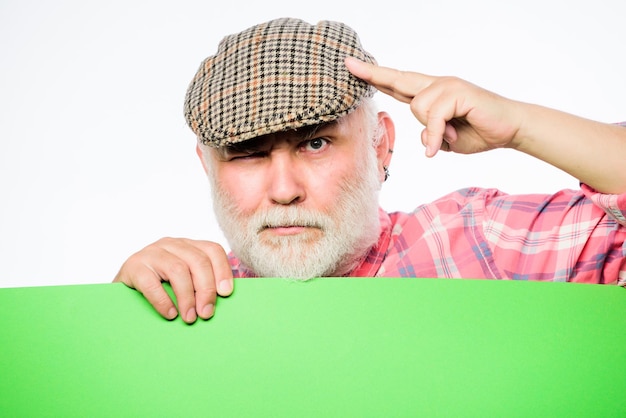 Zdjęcie starszy brodaty mężczyzna zerknąć z banera miejsce ogłoszenie emeryt dziadek w kapeluszu vintage trzymać plakat informacje kopia przestrzeń ogłoszenie o wydarzeniu koncepcja ogłoszenia reklama sklep