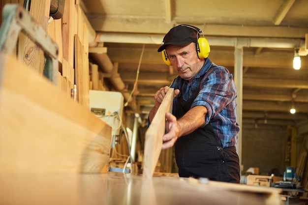 Starszy cieśla w mundurach pracuje na maszynie do obróbki drewna w zakładzie stolarskim
