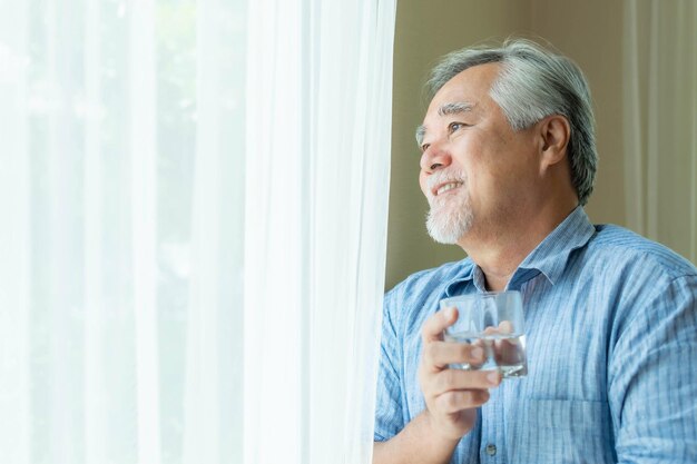Starszy człowiek stary człowiek czuje się szczęśliwy, pijąc świeżą wodę rano, ciesząc się czasem w swoim domu w tle wnętrza styl życia koncepcja szczęścia seniora