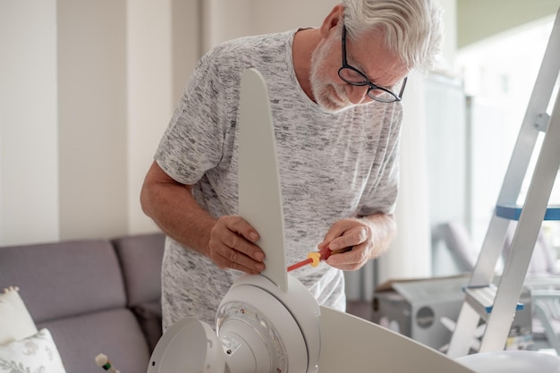 Starszy doświadczony elektryk pracuje nad zainstalowaniem wentylatora łopatkowego na suficie w domu