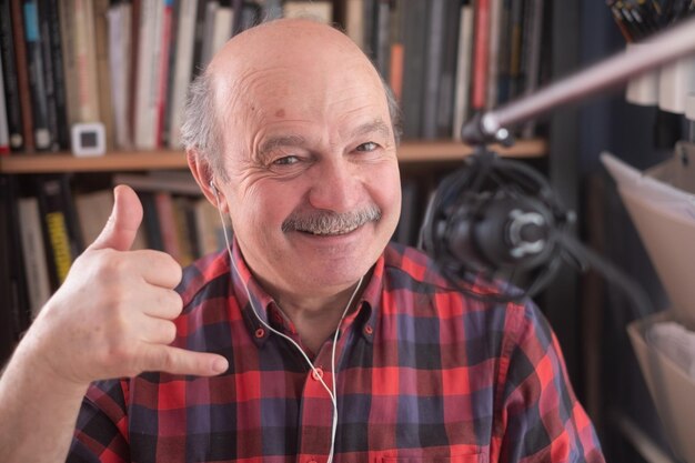 Starszy emerytowany blogger patrzący na vlog z kamerą pokazujący gest „zadzwoń do mnie”