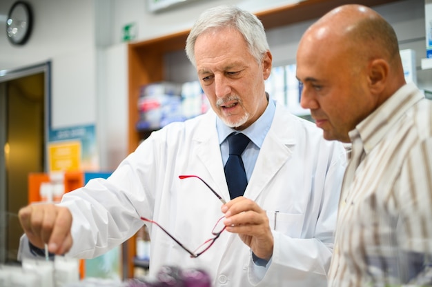 Starszy farmaceuta zajmujący się klientem, oboje noszący maski z powodu koronawirusa