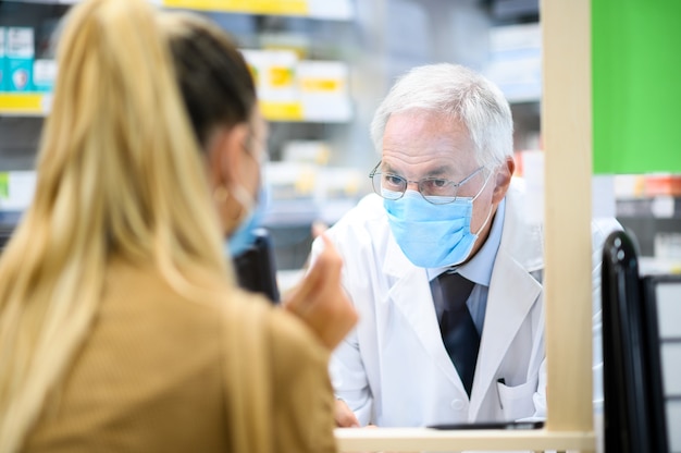 Starszy farmaceuta zajmujący się klientem, oboje noszący maski z powodu koronawirusa