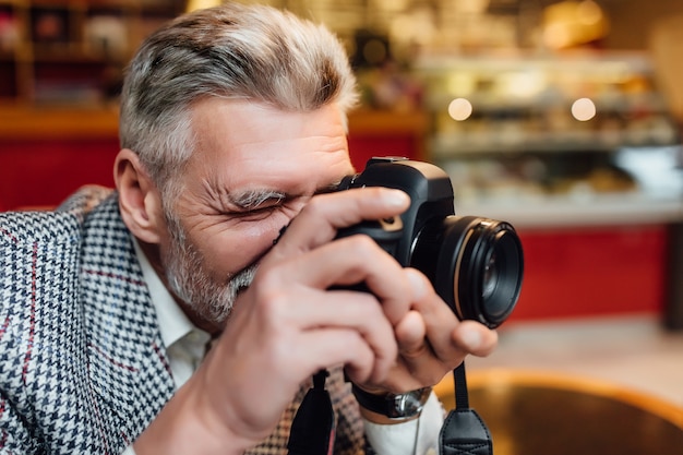 Starszy fotograf trzyma stary aparat fotograficzny i robi zdjęcie w nowoczesnej stołówce.