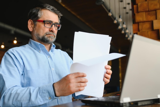 Starszy freelancer pracujący na laptopie w koncepcji pracy zdalnej w kawiarni