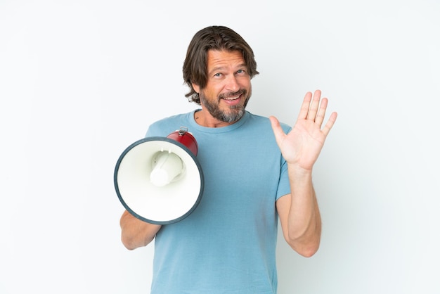 Starszy holenderski mężczyzna na białym tle trzymający megafon i pozdrawiający ręką ze szczęśliwym wyrazem twarzy