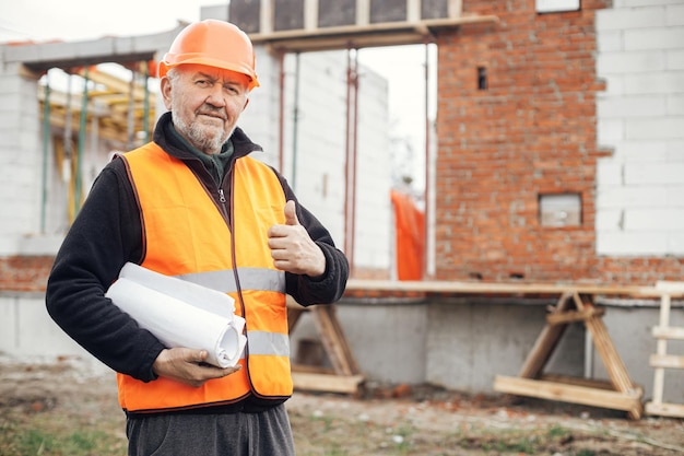 Starszy inżynier lub pracownik budowlany w kasku zatwierdzający budowę nowego nowoczesnego domu z planami Portret męskiego architekta lub wykonawcy posiadającego plany na budowie