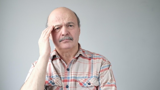 Starszy kaukaski mężczyzna pokazuje, jak bardzo boli go głowa, doświadczając bólu
