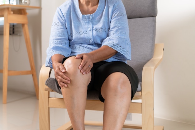 Starszy kobieta cierpi na ból kolana w domu, pojęcie problemu zdrowotnego