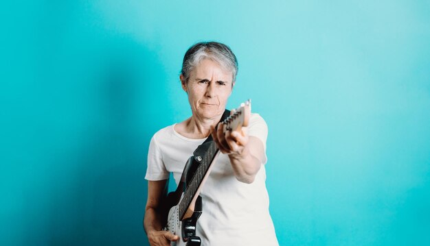 Starszy kobieta gra na gitarze elektrycznej. Zamknij się portret pięknej starej kobiety gra na gitarze elektrycznej na niebieskim tle. Nauka nowych hobby.