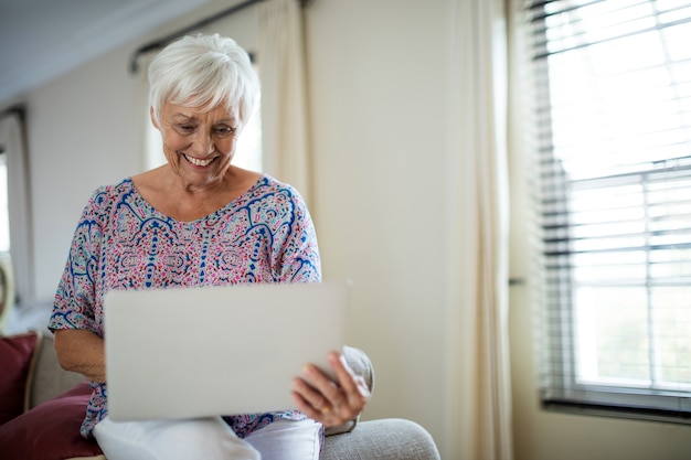 Starszy kobieta za pomocą laptopa w salonie w domu
