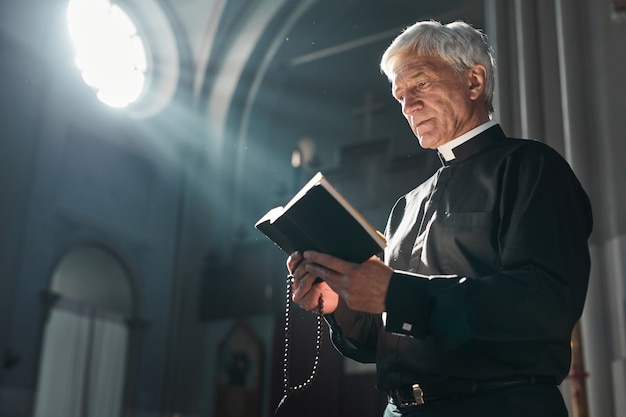 Starszy ksiądz czyta Biblię podczas ceremonii stojąc w kościele