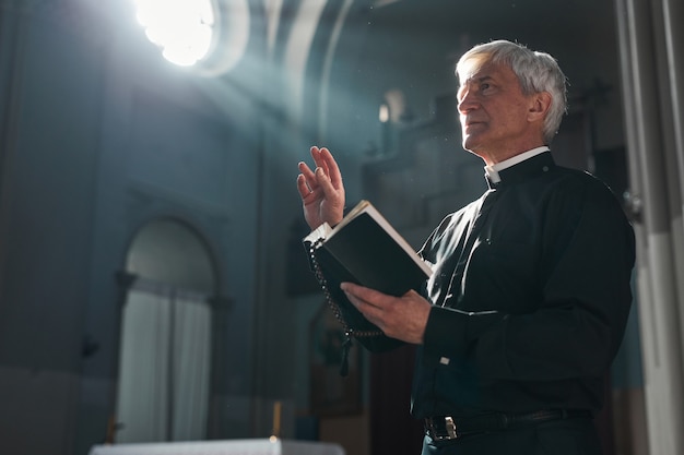 Starszy ksiądz stojący z Biblią podczas ceremonii w kościele