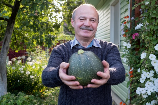 Starszy latynoski mężczyzna trzyma świeżą sezonową zieloną cukinię uśmiechając się będąc zadowolonym