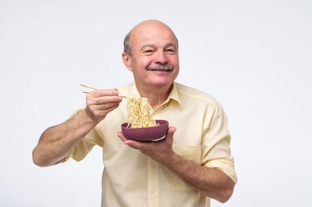Starszy łysy azjatycki mężczyzna je makaron tradycyjne chińskie jedzenie
