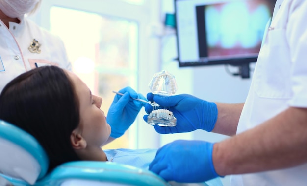 Starszy mężczyzna dentysta w gabinecie stomatologicznym rozmawia z pacjentką i przygotowuje się do leczenia