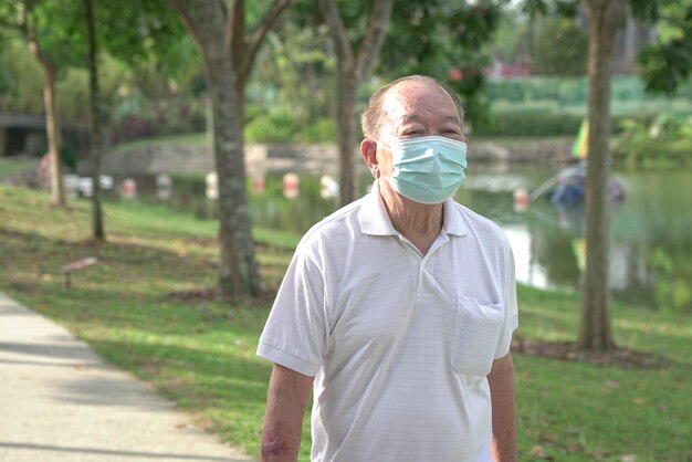 Starszy mężczyzna noszący maskę na twarz spacerujący po parku
