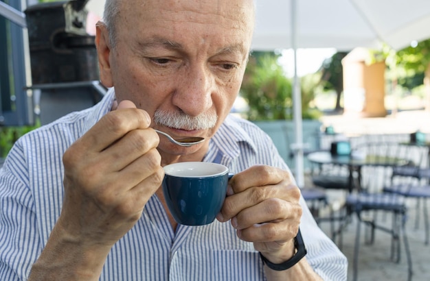 Starszy mężczyzna pijący kawę espresso w kawiarni na świeżym powietrzu