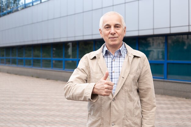 Starszy mężczyzna pokazuje kciuki do góry na zewnątrz w krajobraz miasta, w pobliżu budynków biurowych