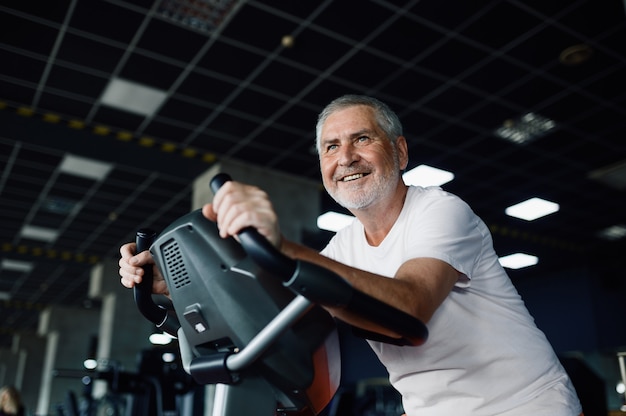 Starszy mężczyzna pozuje na rowerze stacjonarnym w siłowni