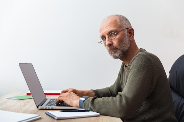 Starszy mężczyzna pracuje na laptopie i patrzy na kamerę