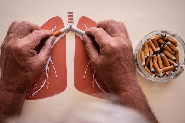 Starszy mężczyzna rasy kaukaskiej trzymający złamany papieros w rękach Popielniczka pełna niedopałków Rzuć palenie Papierosy nikotyna uszkadzają płuca zrujnowane przez dym Świat dzień bez tytoniu